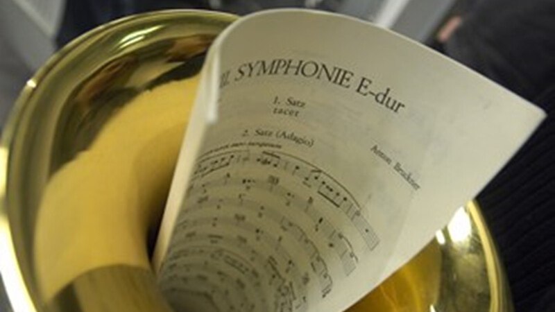 Ein Notenblatt der Symphonie E-Dur von Anton Bruckner steckt in einem Horn. Der Fokus liegt auf der Partitur und dem Instrument., © Württembergische Staatstheater Stuttgart