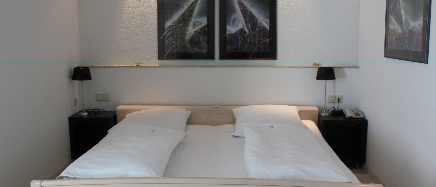 A hotel room with a double bed, two nightstands with lamps, and abstract paintings on the wall., &copy; Hotel Spahr
