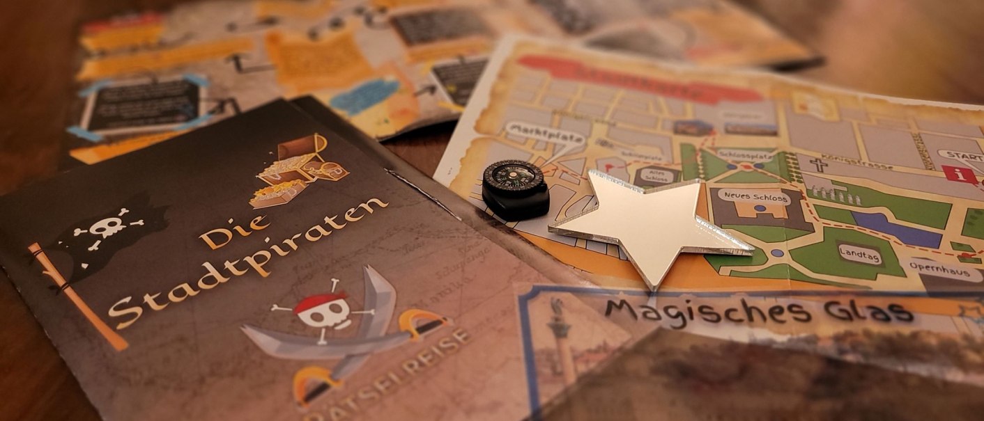 Ein Brettspiel mit dem Titel 'Die Stadtpiraten', Karten, ein Kompass und ein Stern liegen auf einem Tisch. Es scheint ein Rätselspiel zu sein., © SMG