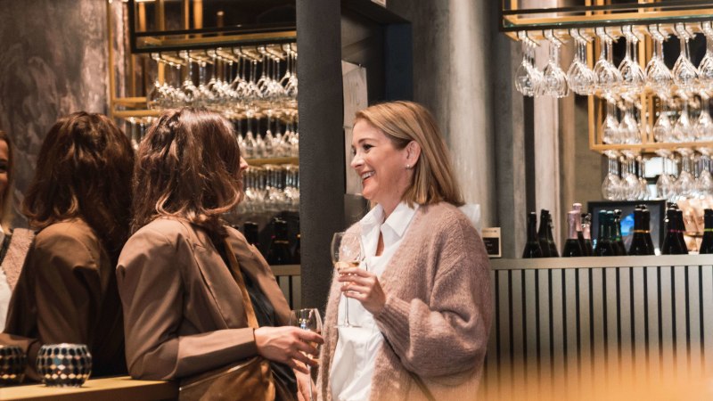 Four women are chatting in a stylish bar, holding champagne glasses. Glasses hang in the background, bottles stand on the bar., © Stuttgart-Marketing GmbH, wpsteinheisser