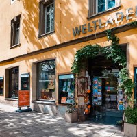 Exterior view of the Planie world store with a yellow façade, large windows and an entrance decorated with plants., © Michael Latz Exterior view of the Planie world store with a yellow façade, large windows and an entrance decorated with plants., © Michael Latz