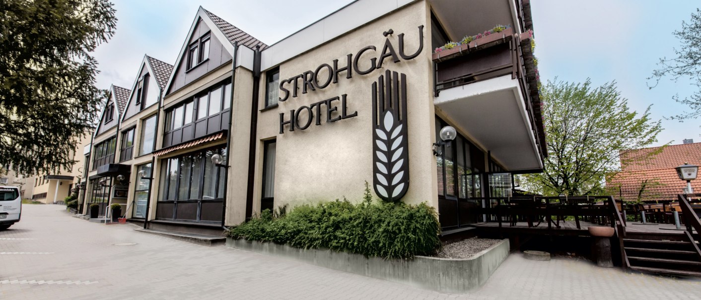 Außenansicht des Strohgäu Hotels mit moderner Fassade, großen Fenstern und einem Balkon. Ein Baum und ein geparkter Van sind sichtbar., © Novum Management GmbH Außenansicht des Strohgäu Hotels mit moderner Fassade, großen Fenstern und einem Balkon. Ein Baum und ein geparkter Van sind sichtbar., © Novum Management GmbH