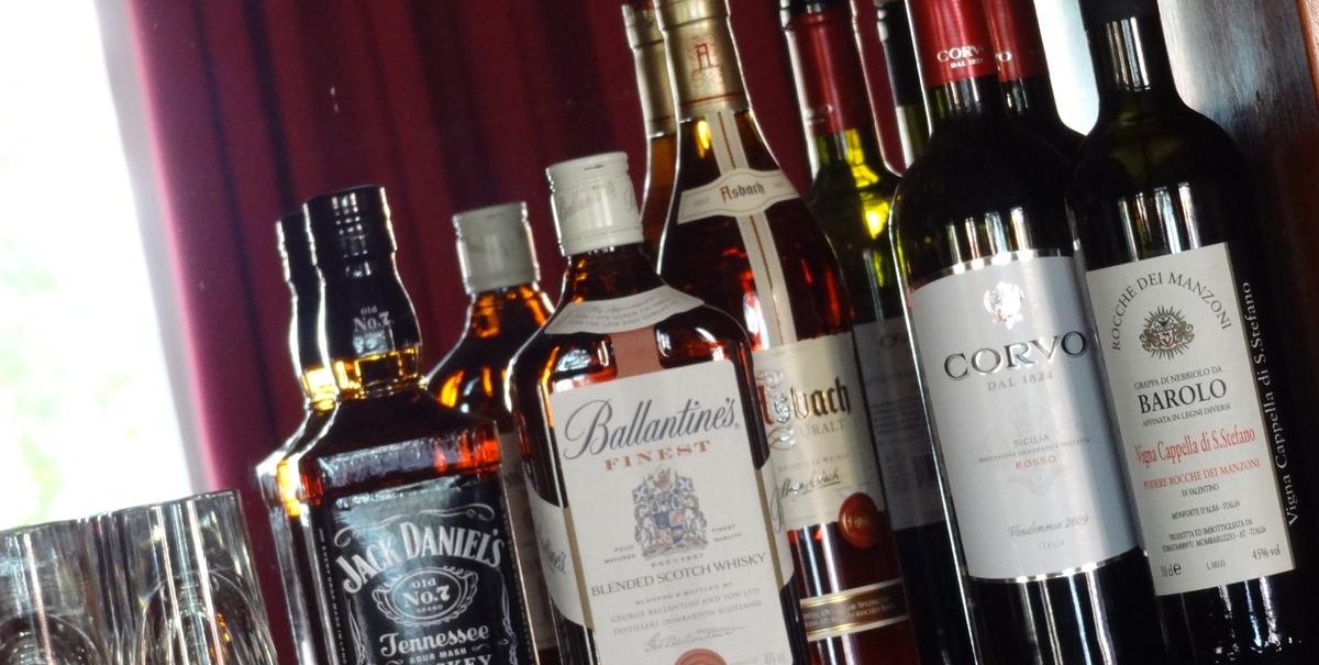 Verschiedene Whisky- und Weinflaschen stehen auf einem Regal vor einem roten Vorhang. Links sind Gläser zu sehen., © Hotel Arcis