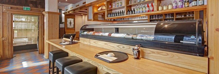 A Japanese restaurant with a sushi counter, bar stools and shelves full of sake bottles. Wooden elements dominate the interior., &copy; Martin Frey
