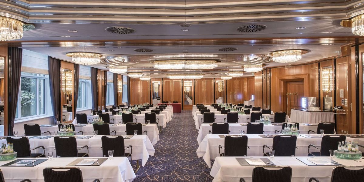 Elegant meeting room with white tablecloths, black chairs and chandeliers. Wooden walls and large windows create a stylish atmosphere., © Maritim Hotelgesellschaft mbH Elegant meeting room with white tablecloths, black chairs and chandeliers. Wooden walls and large windows create a stylish atmosphere., © Maritim Hotelgesellschaft mbH