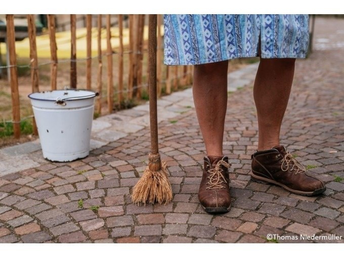 Beine einer Person in braunen Schuhen und blauem Rock, mit Besen und weißem Eimer auf Kopfsteinpflaster., © Stuttgart Marketing GmbH Beine einer Person in braunen Schuhen und blauem Rock, mit Besen und weißem Eimer auf Kopfsteinpflaster., © Stuttgart Marketing GmbH