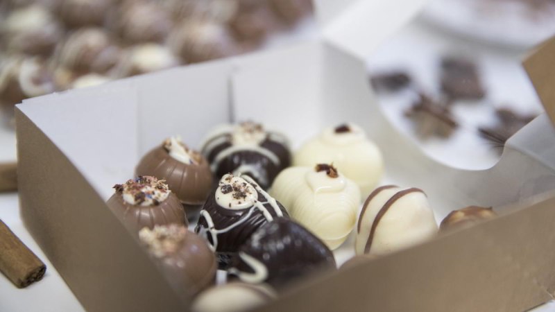 Eine Schachtel mit handgemachten Pralinen in verschiedenen Schokoladensorten, dekoriert mit Streuseln und Mustern., © hoponopo GmbH