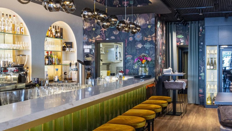 Eleganter Gastraum mit Marmortheke, gelben Hockern und stilvoller Beleuchtung. Die Bar ist gut bestückt, mit Gläsern und Flaschen dekoriert., © SMG, Sarah Schmid