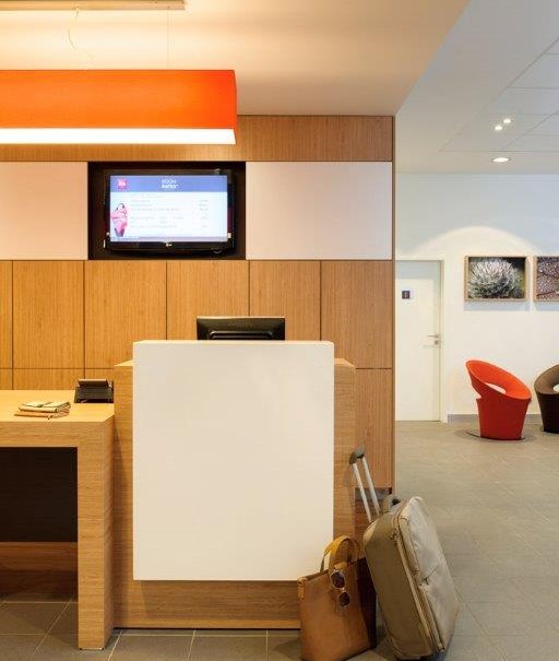 Eine moderne Hotelrezeption mit Holzverkleidung, Bildschirm, roter Lampe und Gepäckstücken auf dem Boden., © TOMAS Eine moderne Hotelrezeption mit Holzverkleidung, Bildschirm, roter Lampe und Gepäckstücken auf dem Boden., © TOMAS