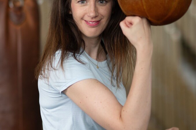Eine Frau in einem Fitnessstudio posiert mit einem Boxsack. Sie tr&auml;gt ein hellblaues T-Shirt und l&auml;chelt in die Kamera., &copy; Theaterhaus Stuttgart e.V.