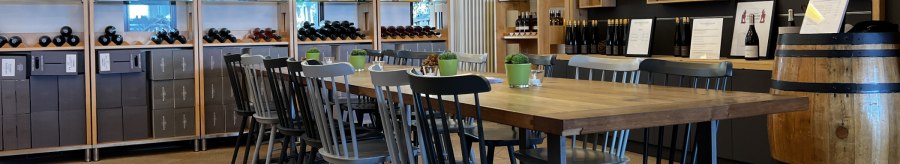 Wine bar with wooden table and chairs, surrounded by wine racks and decorations. Bright, inviting atmosphere with wine bottles and plants., &copy; Weinfactum Bad Cannstatt