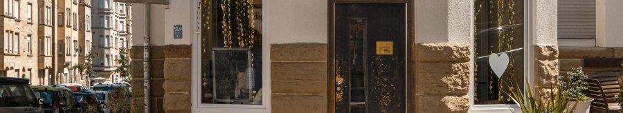 Eingang des Café Seyffer’s an einer Straßenecke, dekoriert mit goldenen Girlanden und Pflanzen. Die Straße ist von Wohnhäusern gesäumt., © SMG, Sarah Schmid