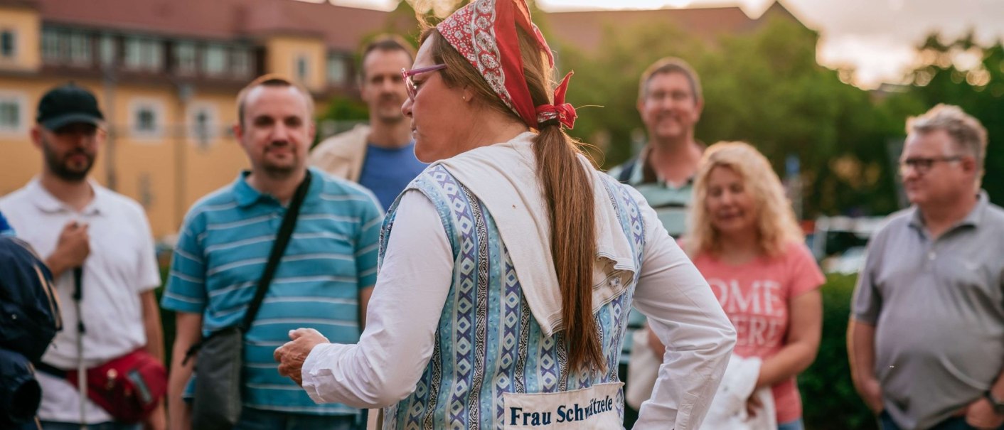 Eine Frau mit Kopftuch und Brille spricht zu einer Gruppe von Menschen im Freien. Sie trägt eine Weste mit der Aufschrift 'Frau Schwitzele'., © Thomas Niedermüller Eine Frau mit Kopftuch und Brille spricht zu einer Gruppe von Menschen im Freien. Sie trägt eine Weste mit der Aufschrift 'Frau Schwitzele'., © Thomas Niedermüller