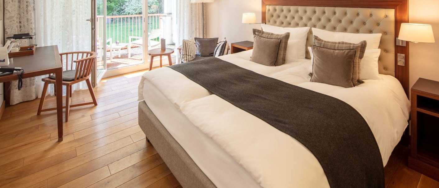 Elegantes Hotelzimmer mit großem Bett, Holzboden, Schreibtisch und Balkon mit Blick ins Grüne., © Waldhotel Stuttgart GmbH