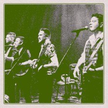 Four musicians stand on a stage and play instruments. They are singing into microphones. The image has a green filter., &copy; see on the left