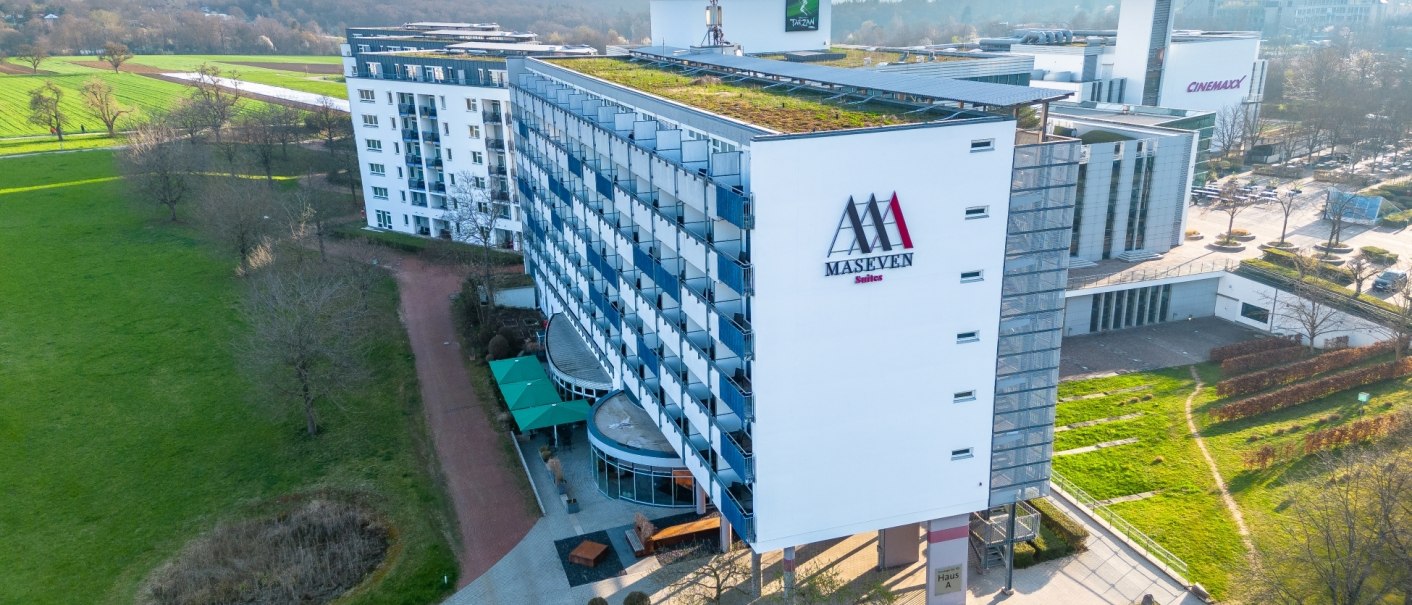 Luftaufnahme des MASEVEN Hotels im SI-Centrum Stuttgart, umgeben von Grünflächen und nahegelegenen Gebäuden., © MASEVEN Stuttgart SI-Centrum