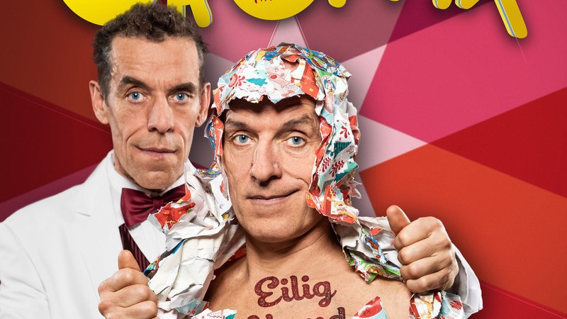 Zwei M&auml;nner, einer in einem wei&szlig;en Anzug, der andere in Geschenkpapier eingewickelt, mit dem Schriftzug 'Eilig Abend' auf der Brust. Bunter, gestreifter Hintergrund., &copy; Theaterhaus Stuttgart e.V.
