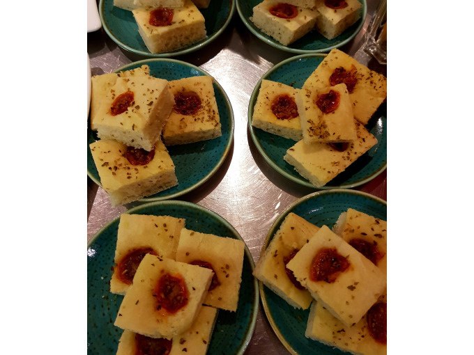Small pieces of focaccia with tomatoes and herbs arranged on several green plates., © Kultweine-Kochwelten-Kunstücke - Kochschule Sonja Lenz Small pieces of focaccia with tomatoes and herbs arranged on several green plates., © Kultweine-Kochwelten-Kunstücke - Kochschule Sonja Lenz