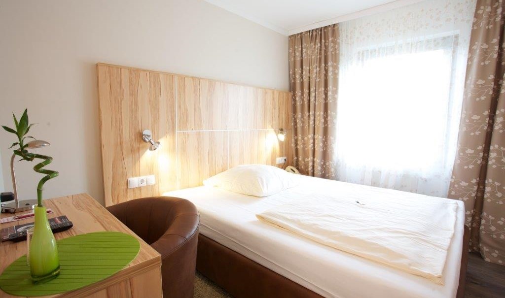 A cozy single room with a bed, a desk, an armchair and a window with patterned curtains., © Hotel Reinhardtshof Garni A cozy single room with a bed, a desk, an armchair and a window with patterned curtains., © Hotel Reinhardtshof Garni