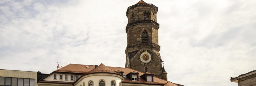 Tower of the collegiate church in Stuttgart with clock and weathercock, surrounded by buildings under a cloudy sky., © SMG Stuttgart Marketing GmbH - Sarah Schmid Tower of the collegiate church in Stuttgart with clock and weathercock, surrounded by buildings under a cloudy sky., © SMG Stuttgart Marketing GmbH - Sarah Schmid
