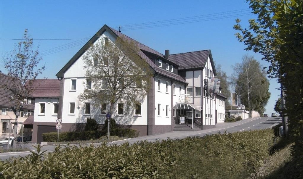 Das Hotel Waldhorn in Böblingen liegt an einer Straße, umgeben von Bäumen und Sträuchern. Es hat ein traditionelles Design mit weißen Wänden und dunklem Dach., © Hotel Waldhorn