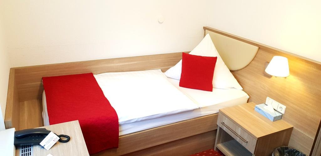 Ein gemütliches Einzelzimmer mit einem Bett, rotem Überwurf und Kissen. Ein Nachttisch mit Lampe und Telefon ist vorhanden., © Aparthotel Wangener Landhaus Ein gemütliches Einzelzimmer mit einem Bett, rotem Überwurf und Kissen. Ein Nachttisch mit Lampe und Telefon ist vorhanden., © Aparthotel Wangener Landhaus