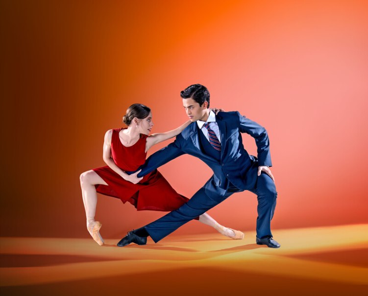 Ein Tänzerpaar in eleganter Pose, sie im roten Kleid, er im Anzug, vor einem orangefarbenen Hintergrund. Beide blicken sich intensiv an., © Württembergische Staatstheater Stuttgart