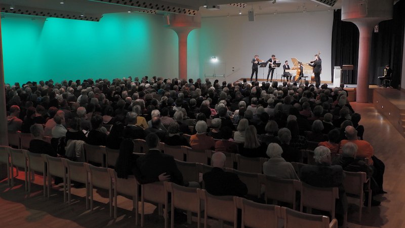 Ein Konzertsaal mit vielen Zuschauern. Auf der Bühne spielen Musiker klassische Instrumente. Die Beleuchtung ist grün und rot., © Internationale Hugo-Wolf-Akademie Ein Konzertsaal mit vielen Zuschauern. Auf der Bühne spielen Musiker klassische Instrumente. Die Beleuchtung ist grün und rot., © Internationale Hugo-Wolf-Akademie