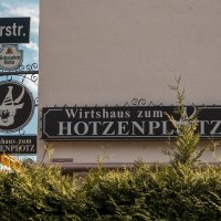 Sign for the Wirtshaus zum Hotzenplotz on Lindensp&uuml;rstra&szlig;e, surrounded by green bushes and a blue sky in the background., &copy; SMG Stuttgart Marketing GmbH - Sarah Schmid