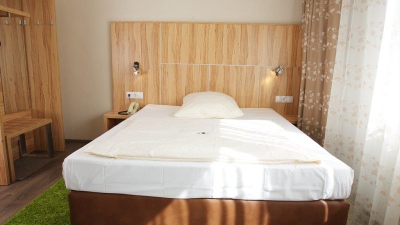 Ein gemütliches Einzelzimmer mit einem Bett, Holzmöbeln und floralen Vorhängen. Ein grüner Teppich liegt auf dem Boden., © Hotel Reinhardtshof Garni