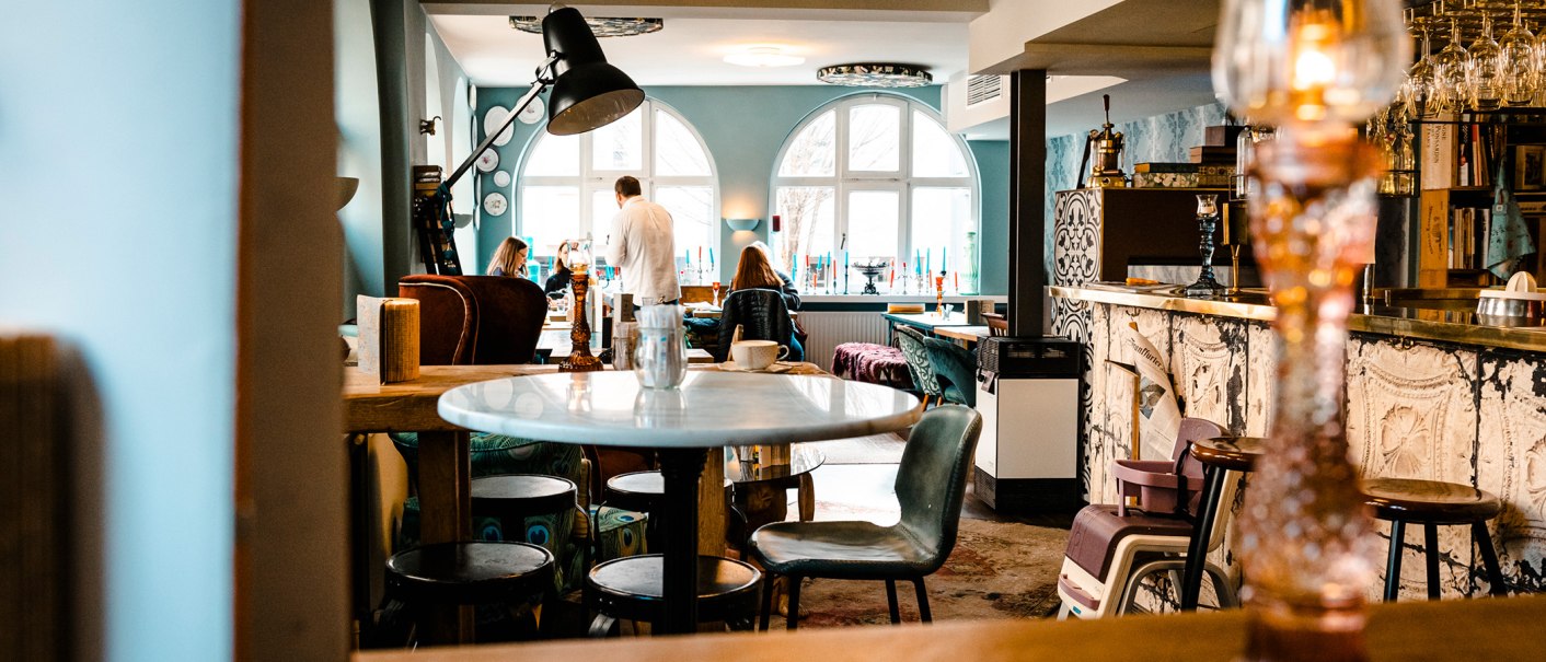 Cozy café with stylish furnishings, round tables and chairs. People sit and chat. Large windows let in light., © SMG Stuttgart Marketing GmbH - Sarah Schmid