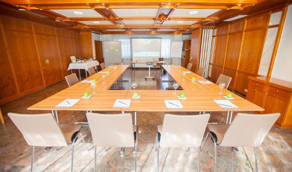 A bright conference room with a U-shaped table, chairs, notepads, and glasses. In the background is a screen and presentation equipment., &copy; Hotel Waldhorn