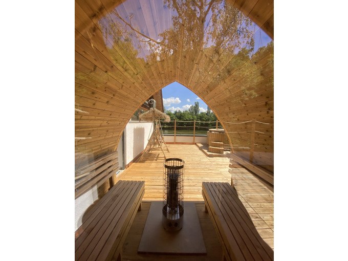 Holzsauna mit gewölbtem Dach, zwei Bänken und einem Ofen. Durch das Fenster sieht man eine Terrasse und Bäume im Hintergrund., © Cool-Tours StattReisen Holzsauna mit gewölbtem Dach, zwei Bänken und einem Ofen. Durch das Fenster sieht man eine Terrasse und Bäume im Hintergrund., © Cool-Tours StattReisen