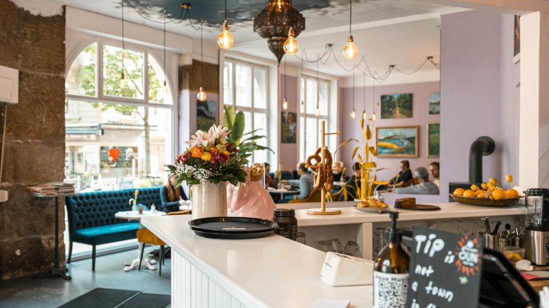 Gem&uuml;tliches Caf&eacute; mit Blumen und Brezeln auf der Theke, blauen Sofas und Kunst an den W&auml;nden. Gro&szlig;e Fenster lassen viel Licht herein., &copy; SMG, Sarah Schmid