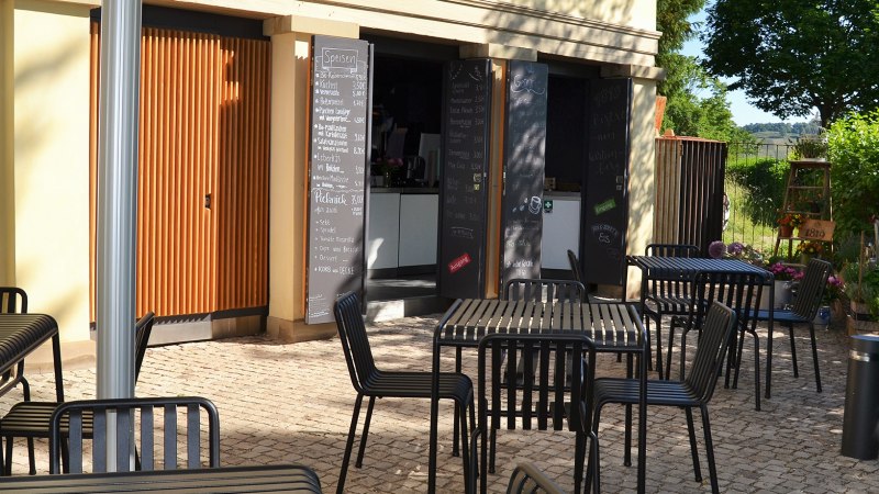 Outdoor area of the 1819 Bistro am Wirtemberg with black tables and chairs on paved ground, surrounded by green vegetation., © 1819 Bistro am Wirtemberg