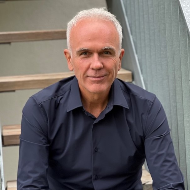 Ein Mann mit grauem Haar und dunklem Hemd sitzt auf einer Treppe und lächelt in die Kamera., © Renitenztheater Stuttgart e.V. Ein Mann mit grauem Haar und dunklem Hemd sitzt auf einer Treppe und lächelt in die Kamera., © Renitenztheater Stuttgart e.V.