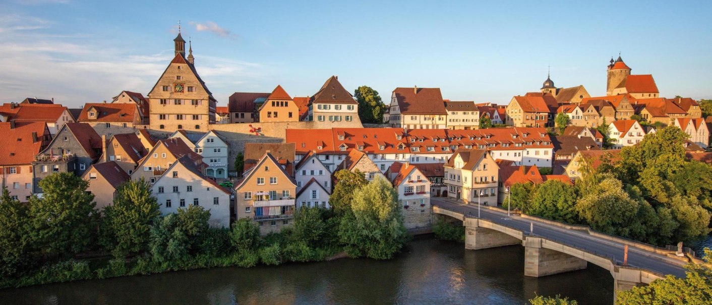 A panoramic view of the picturesque old town of Besigheim with its red roofs and the Enz River in the foreground, bathed in the evening sun., © © Stuttgart-Marketing GmbH A panoramic view of the picturesque old town of Besigheim with its red roofs and the Enz River in the foreground, bathed in the evening sun., © © Stuttgart-Marketing GmbH