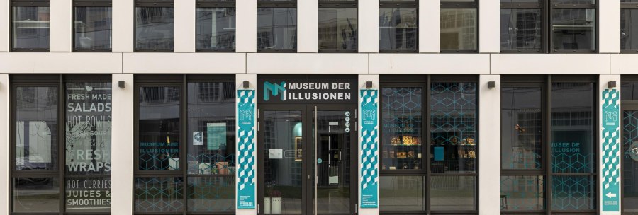 Entrance to the Museum of Illusions in Stuttgart. Modern glass façade with turquoise graphics and lettering. Signs point to the museum., © Stuttgart-Marketing GmbH, Sarah Schmid Entrance to the Museum of Illusions in Stuttgart. Modern glass façade with turquoise graphics and lettering. Signs point to the museum., © Stuttgart-Marketing GmbH, Sarah Schmid