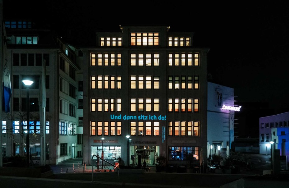 Das Literaturhaus bei Nacht, beleuchtet mit vielen Fenstern. Auf der Fassade steht 'Und dann sitz ich da!'. Rechts ist ein Kino zu sehen., © Literaturhaus