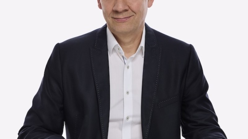 Ein Mann in einem dunklen Anzug sitzt an einem Tisch und h&auml;lt eine Zeitung. Der Hintergrund ist wei&szlig;., &copy; Renitenztheater Stuttgart e.V.