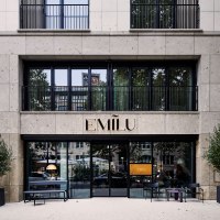 Entrance to the EmiLu Hotel with large glass windows, plants in black pots and the hotel name above the door., &copy; EmiLu Hotel GmbH