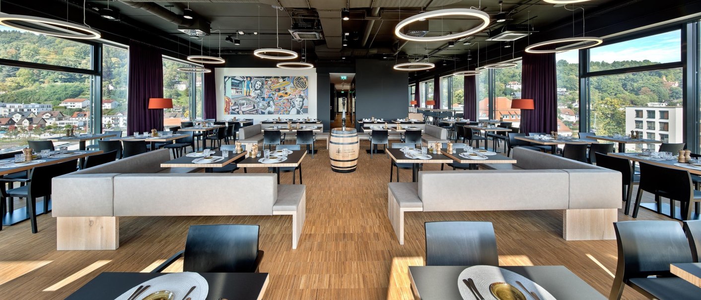 Modern restaurant on the 7th floor with large windows, stylish furniture and a mural. Bright lighting and a view of the city., © Hotel am Remspark Modern restaurant on the 7th floor with large windows, stylish furniture and a mural. Bright lighting and a view of the city., © Hotel am Remspark