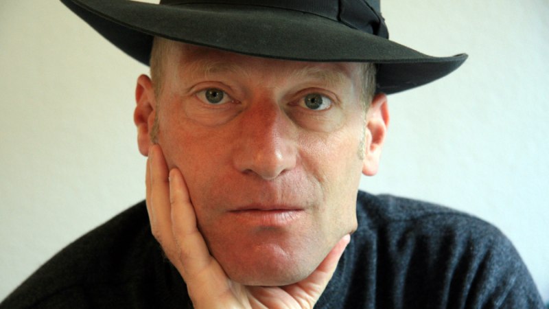 Ein Mann mit schwarzem Hut st&uuml;tzt nachdenklich sein Kinn auf die Hand. Er tr&auml;gt einen dunklen Pullover und blickt direkt in die Kamera., &copy; Foto: Yvonne Berardi