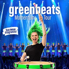 Ein Schlagzeuger mit grünen Haaren trommelt begeistert auf einer Bühne. Im Hintergrund sind weitere Trommler und blaue Lichter zu sehen. "greenbeats Momentum Tour"., © links im Bild