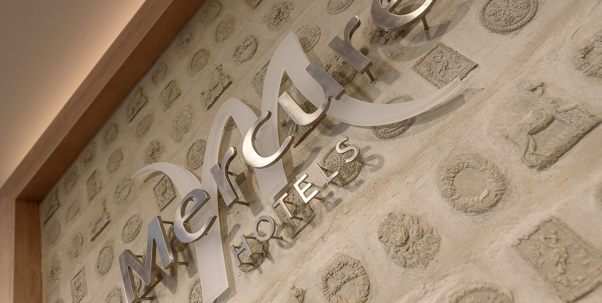Logo von Mercure Hotels an einer Wand mit dekorativen Reliefs und warmem Licht., © TOMAS
