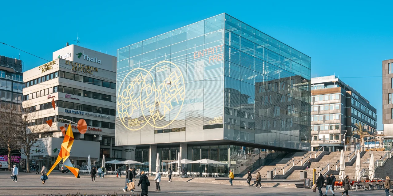 Außenansicht des Kunstmuseums Stuttgart mit gläsernem Kubus, Platz und orangefarbener Skulptur., © SMG, Sarah Schmid Außenansicht des Kunstmuseums Stuttgart mit gläsernem Kubus, Platz und orangefarbener Skulptur., © SMG, Sarah Schmid