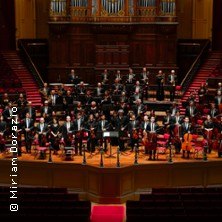 Ein Orchester sitzt auf einer Bühne in einem großen Konzertsaal, bereit für das Jahresschlusskonzert., © links im Bild