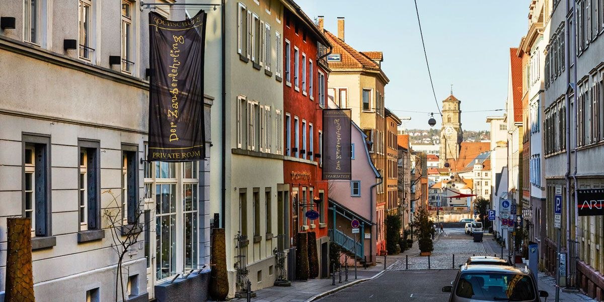 Blick auf eine Straße mit bunten Gebäuden, darunter das Designhotel & Restaurant Der Zauberlehrling. Im Hintergrund ist ein Turm zu sehen., © Designhotel & Restaurant Der Zauberlehrling Blick auf eine Straße mit bunten Gebäuden, darunter das Designhotel & Restaurant Der Zauberlehrling. Im Hintergrund ist ein Turm zu sehen., © Designhotel & Restaurant Der Zauberlehrling