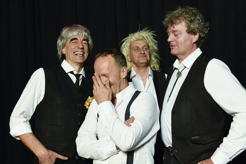 Vier Männer in Anzügen lachen herzlich vor einem schwarzen Hintergrund. Einer hält sich die Hand vors Gesicht, während die anderen lächeln., © Theaterhaus Stuttgart e.V. Vier Männer in Anzügen lachen herzlich vor einem schwarzen Hintergrund. Einer hält sich die Hand vors Gesicht, während die anderen lächeln., © Theaterhaus Stuttgart e.V.