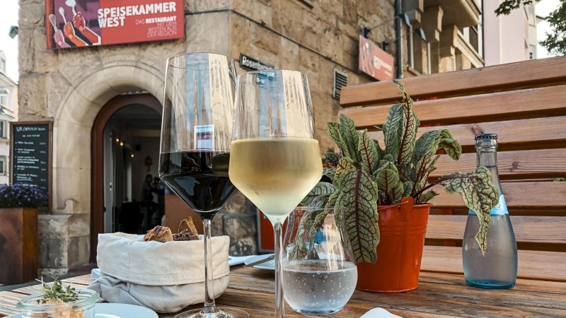 Zwei Weingl&auml;ser und eine Wasserflasche auf einem Tisch vor dem Restaurant 'Speisekammer West'. Im Hintergrund ein steinerner Eingang., &copy; Speisekammer West, Stuttgart